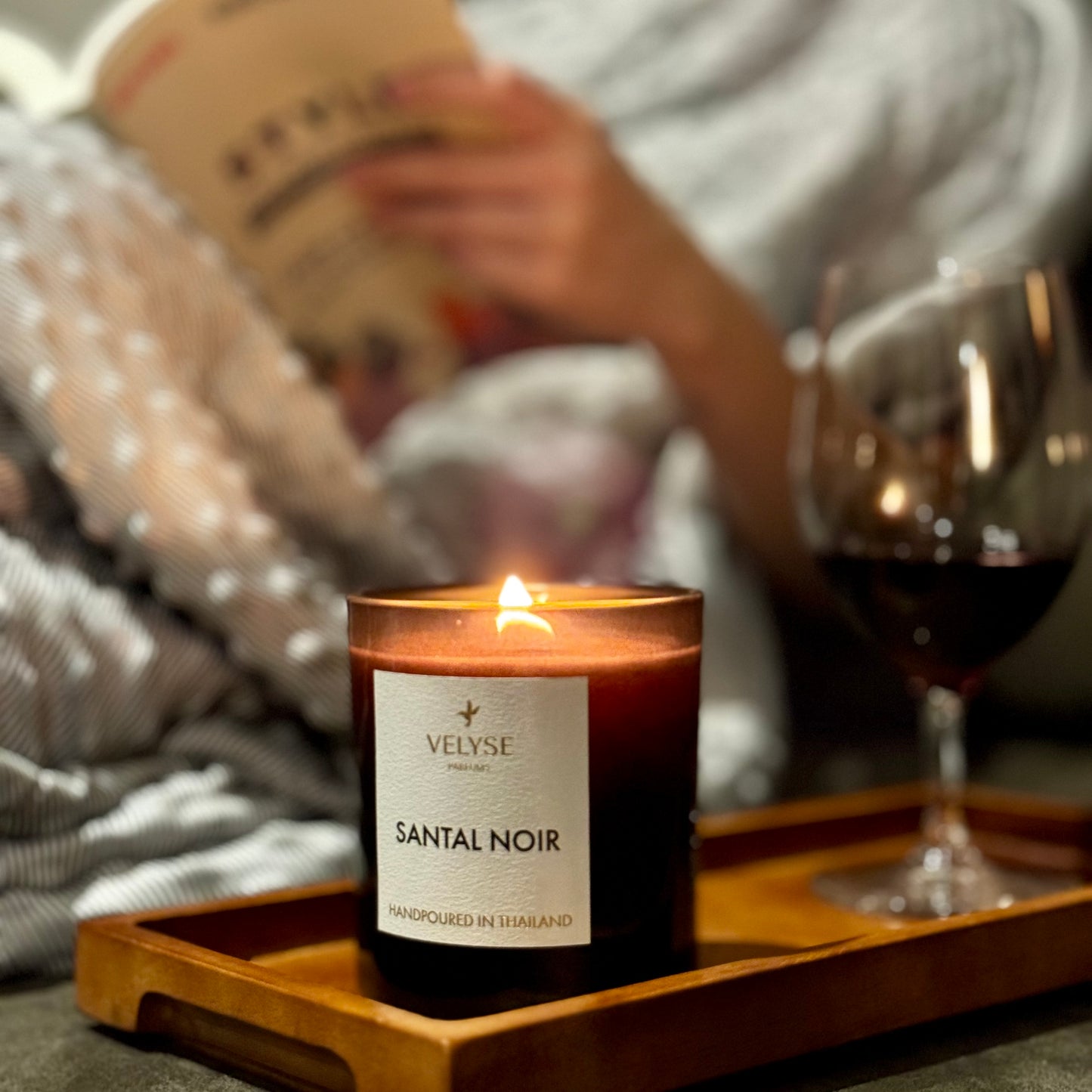 Santal Noir luxury candle burning while relaxing on the couch with a book and wine